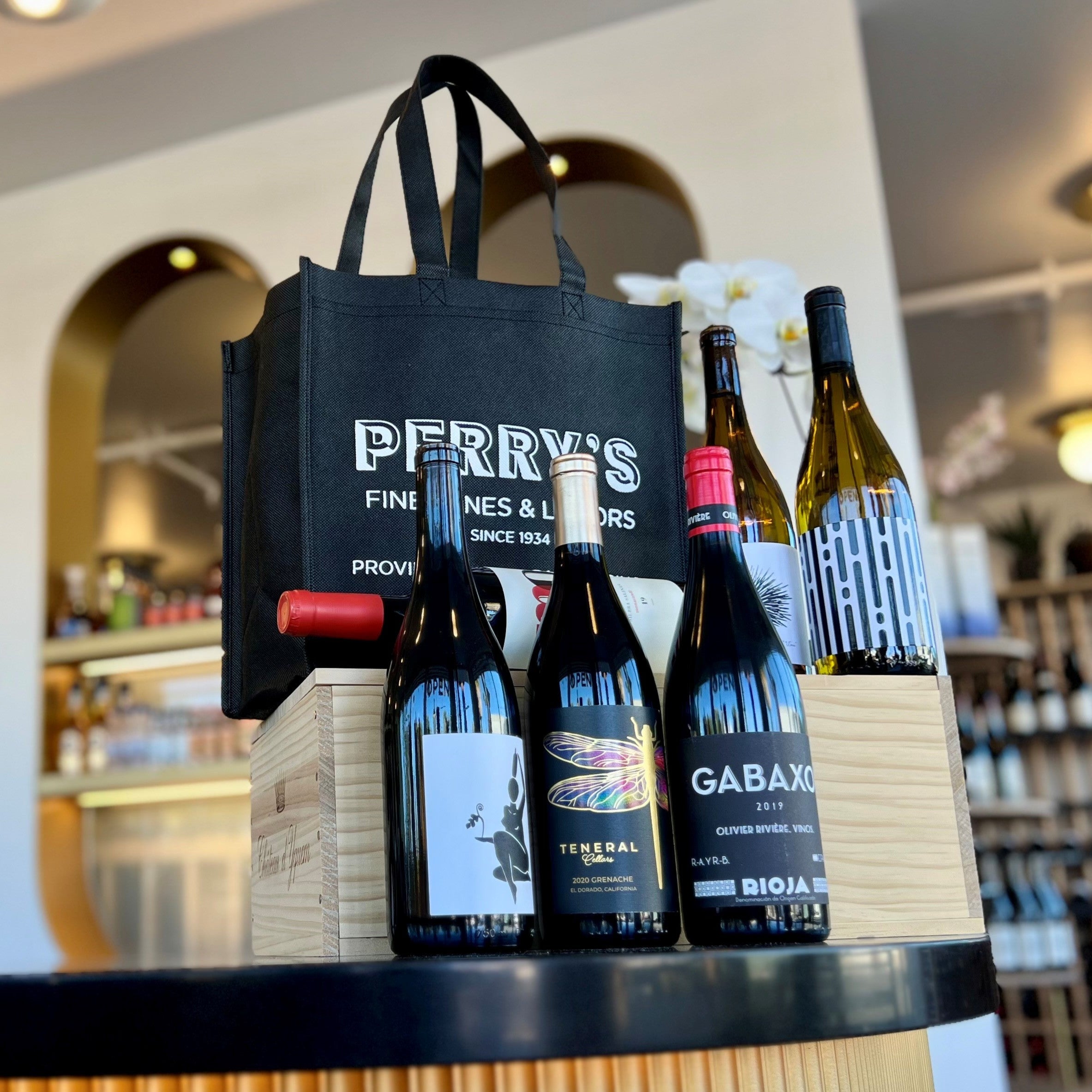 Bottles of wine on a bar counter with a Perry's bag in the foreground.